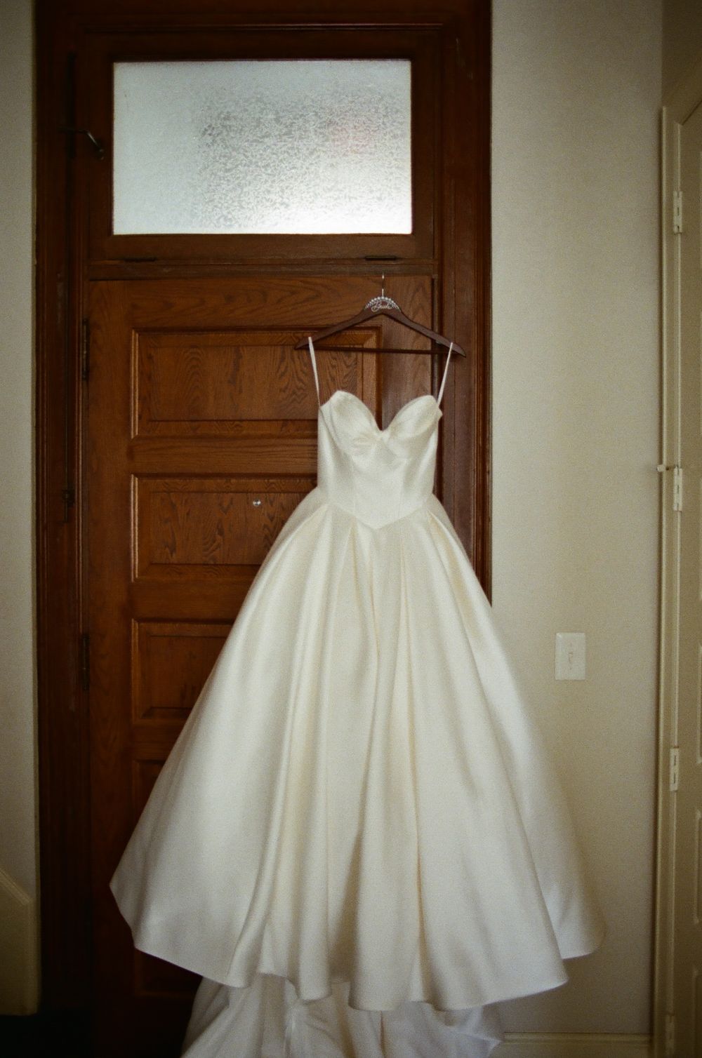 Three elegant white wedding dresses hanging on wooden doors showcase different styles and silhouettes.