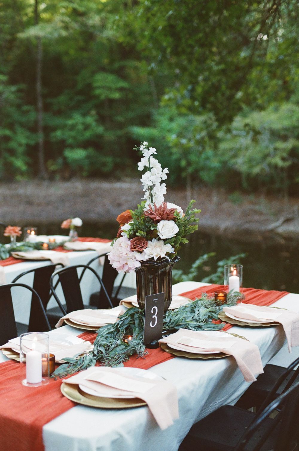 An elegant outdoor wedding reception table setting with white and coral decor against a natural backdrop.