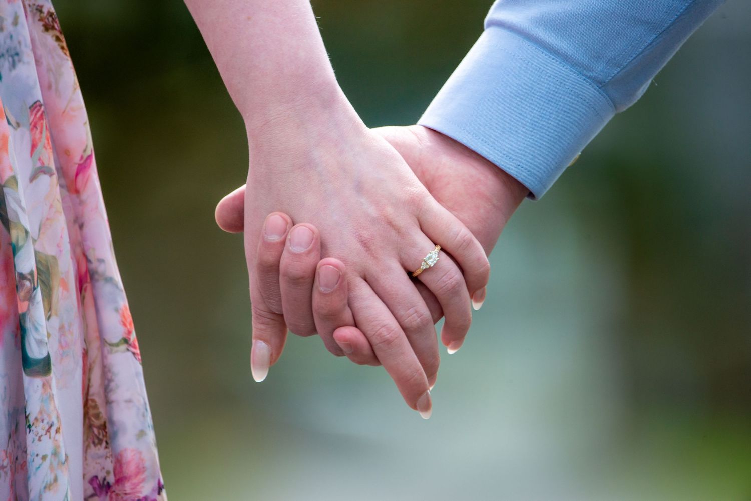 A couple holds hands while wearing floral and blue clothing in an outdoor setting.
