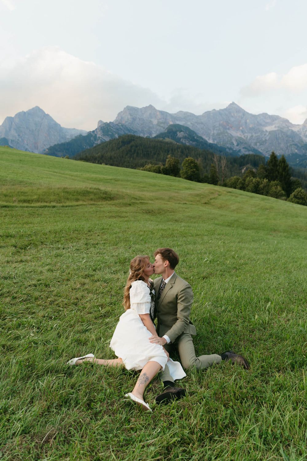 A romantic moment unfolds on an alpine meadow with dramatic mountain scenery in the distance.
