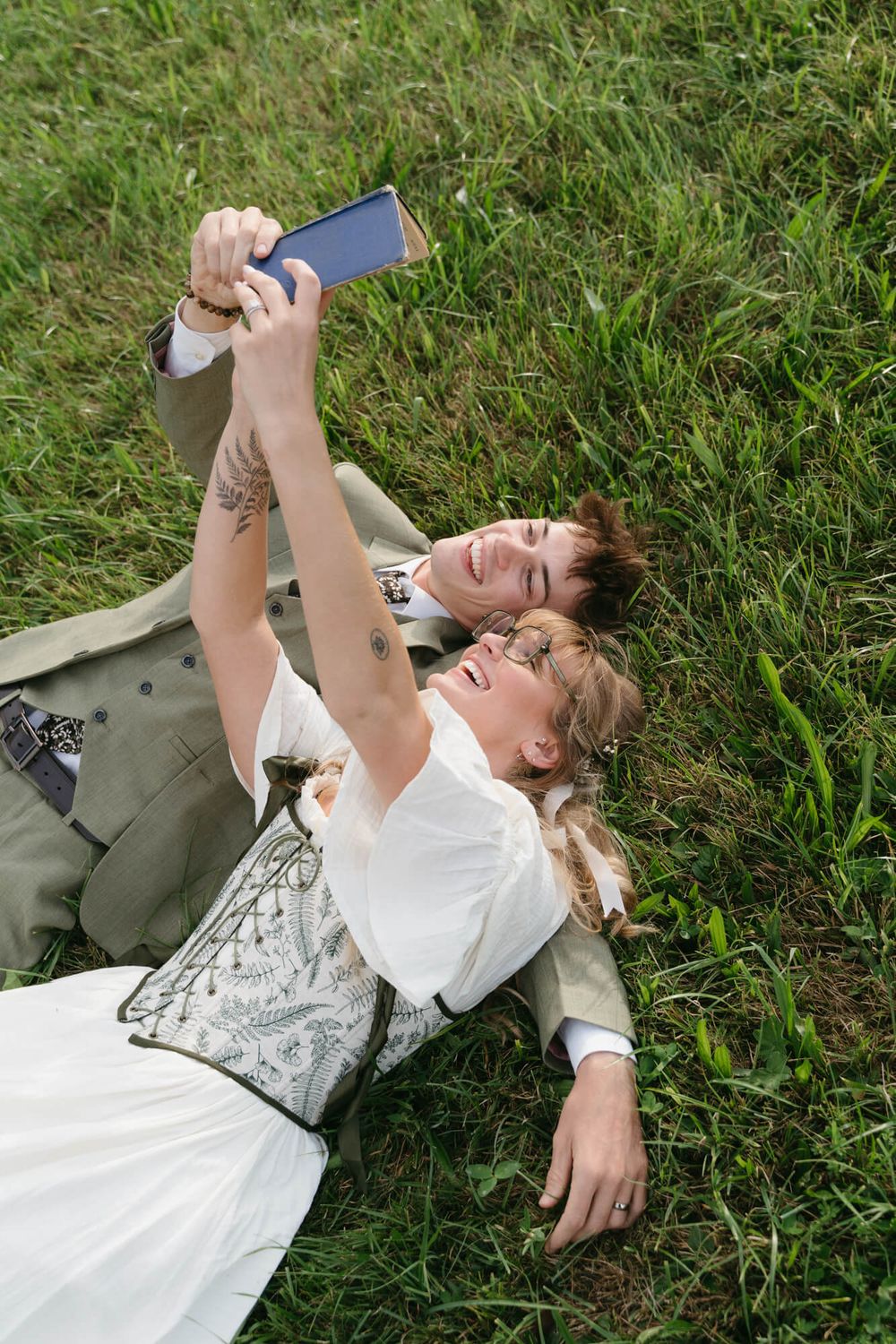 A series of photos showing someone lying in green grass wearing a white dress and olive vest.