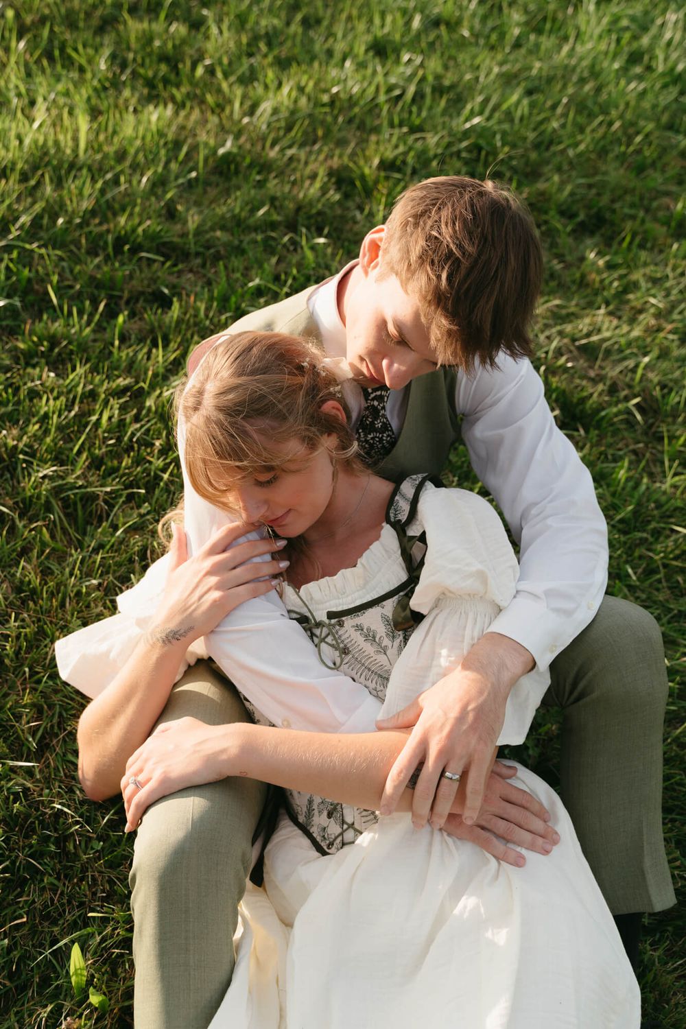 A romantic couple in white and gray embraces intimately on grassy ground in a series of candid photos.