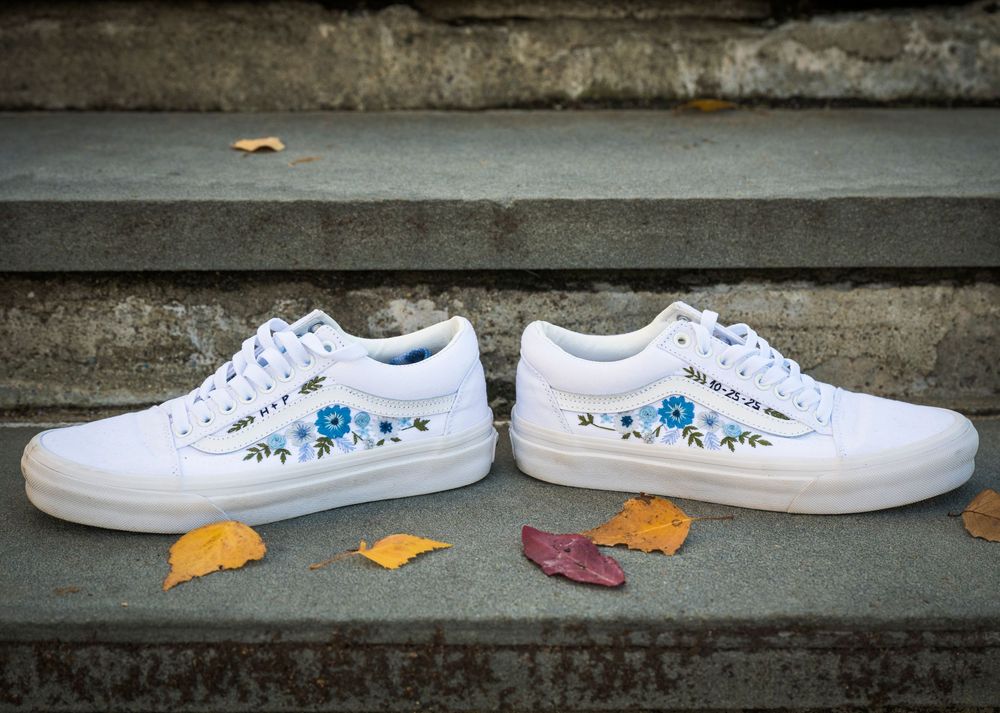 White sneakers with blue floral embroidery and orange price tags arranged in a row on concrete steps.