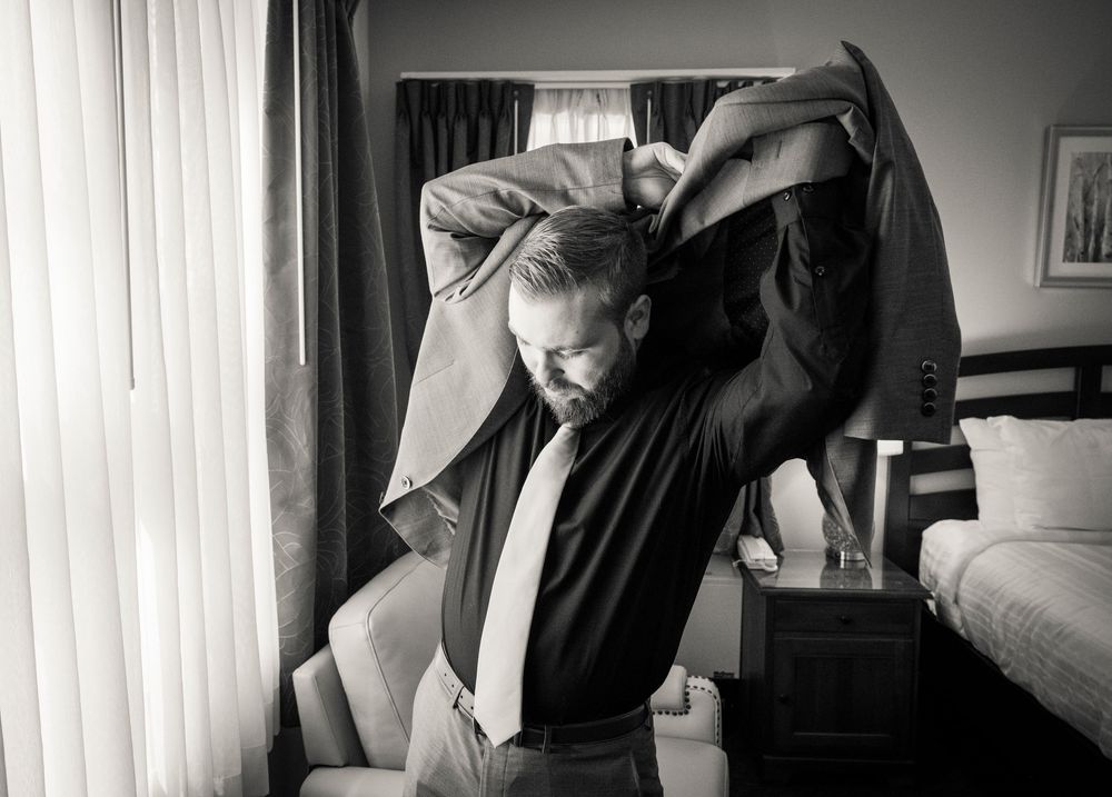 A person in a black shirt stretches their arms overhead while standing near a window in a black and white photograph.