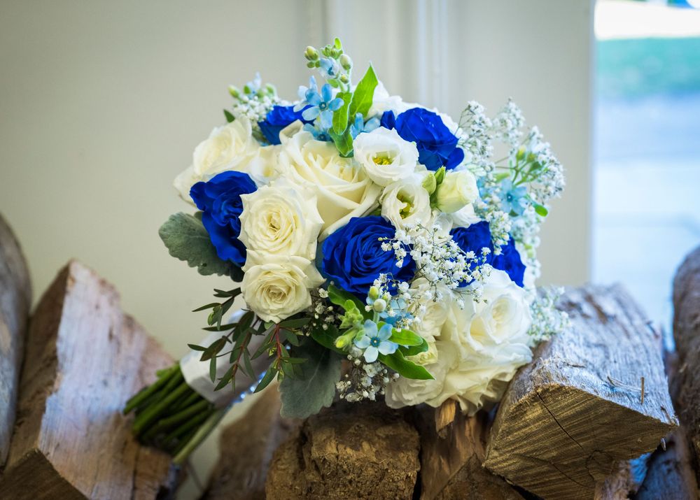 Blue and white wedding bouquet with roses displayed on rustic wood surface.