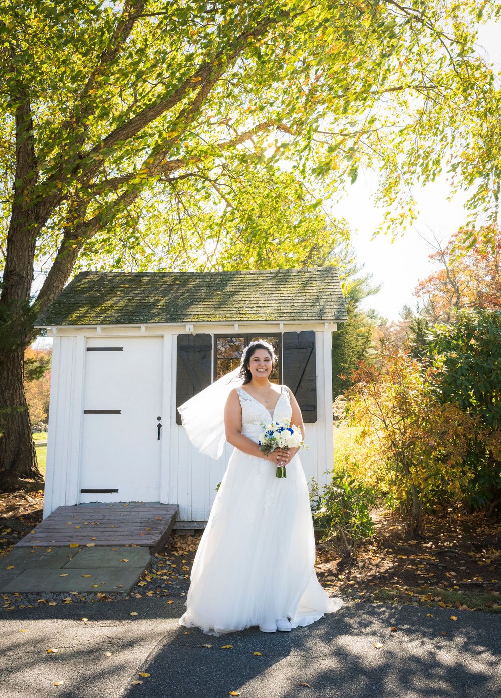 White wedding dress twirls against autumn foliage backdrop near white barn doors.