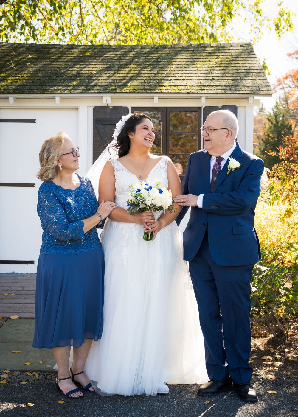 Wedding party in navy and royal blue attire poses together against white building exterior.
