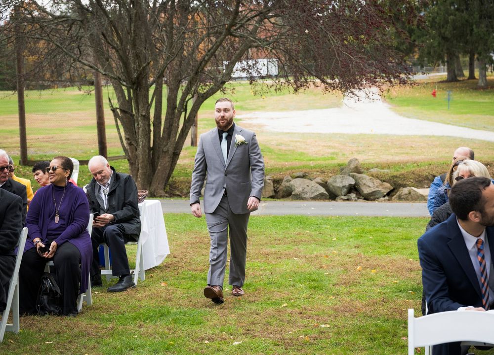 Outdoor wedding ceremony setup with white chairs arranged on a lawn surrounded by trees.