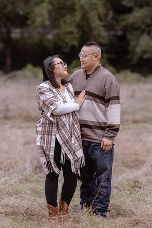 A couple share an intimate moment while standing in a field wearing matching earth-toned outfits.