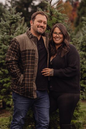 A couple in coordinated fall outfits shares joyful moments together at a Christmas tree farm.