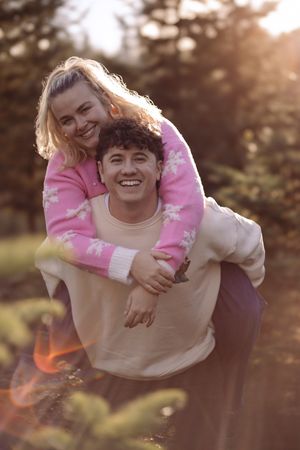 A playful piggyback ride captured during golden hour in a park setting with warm sunlight filtering through trees.