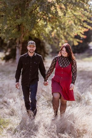 A couple joyfully runs through a field of dried tall grass on a sunny autumn day.