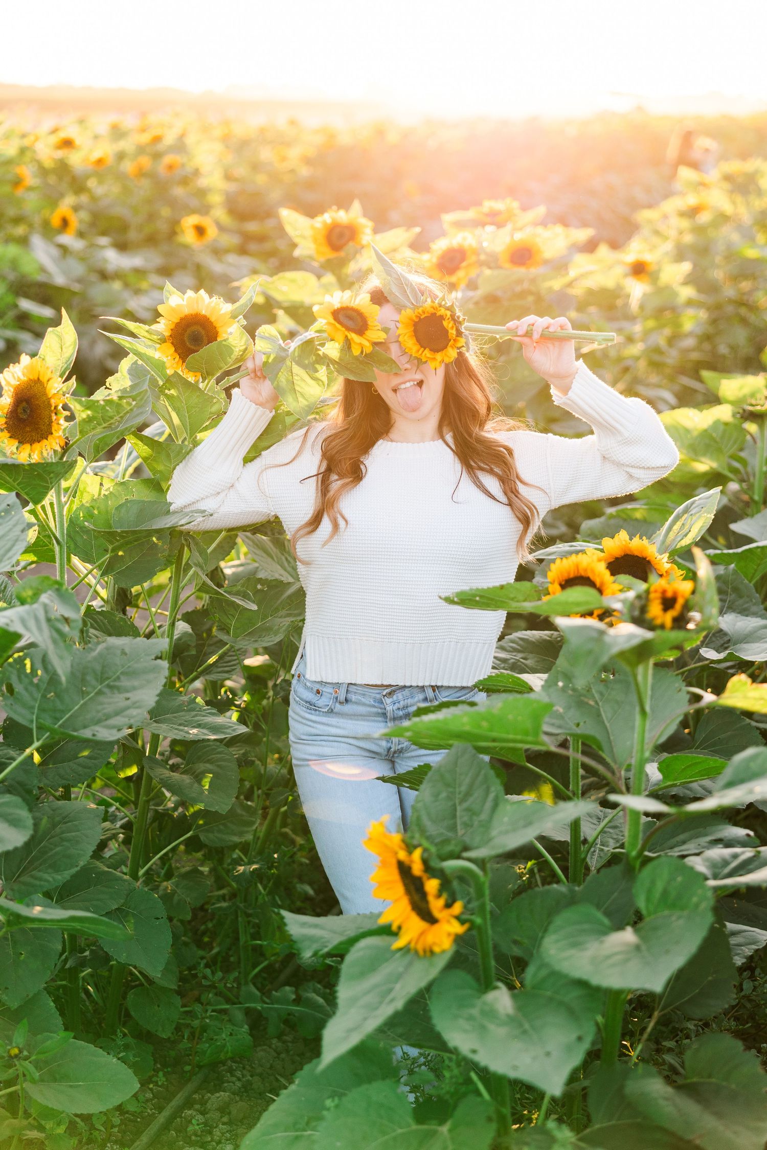 A figure in a white dress stands gracefully among blooming sunflowers at golden hour in a summer garden.
