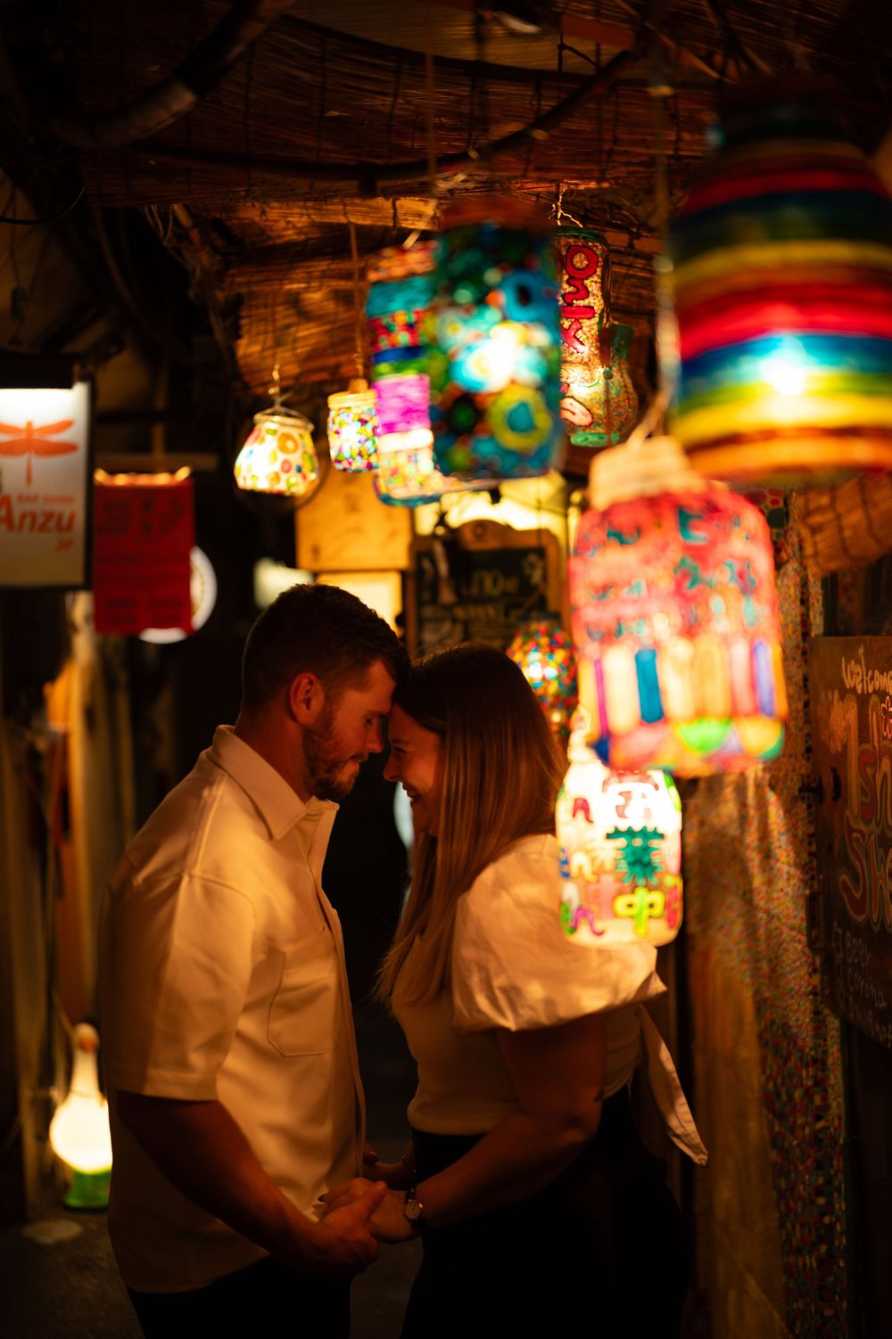 Couple sharing a romantic moment surrounded by colorful hanging lanterns in a warmly lit market alley.