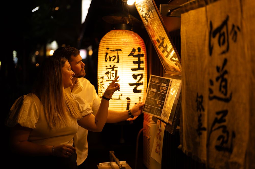Couple admiring a glowing Japanese paper lantern with kanji characters at a night market in Japan.