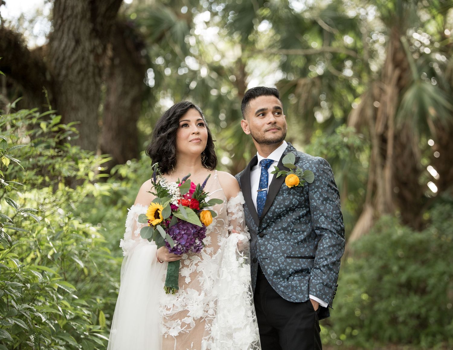 Wedding couple shares an intimate moment surrounded by lush tropical garden foliage at outdoor ceremony.