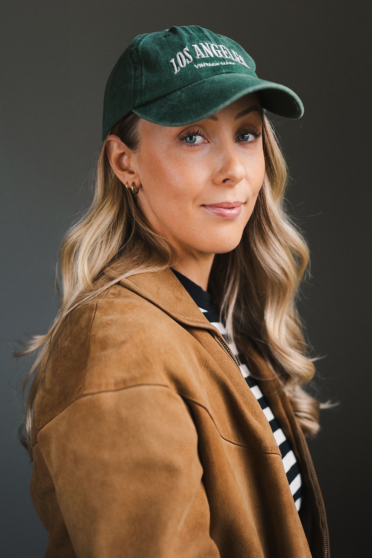 Studioporträtt av fotografen Hanna Göransson iförd grön keps, randig tröja och mockajacka