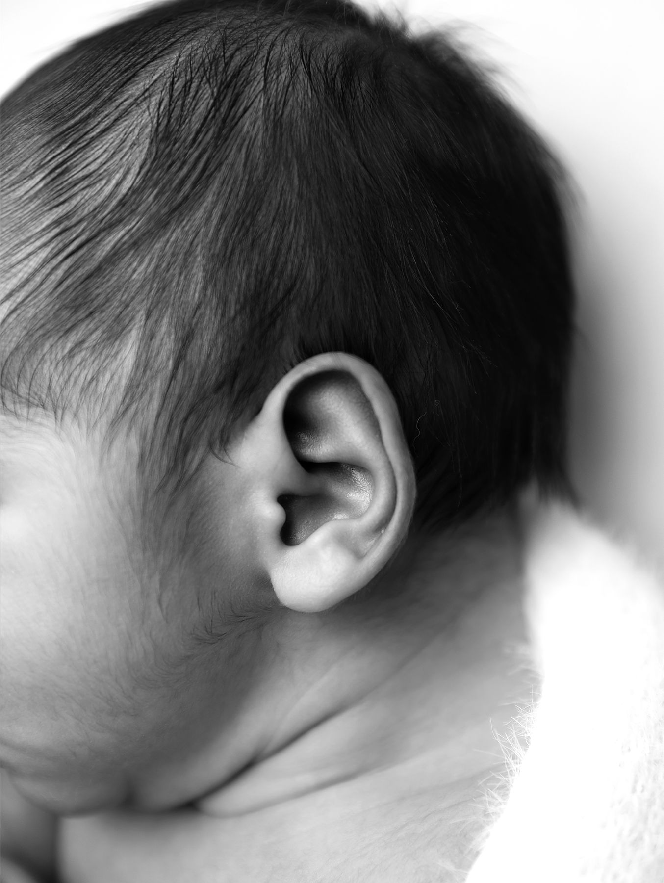 Close-up black and white artistic composition showing an ear and hair detail in soft focus. At a newborn photography studio in Sidcup