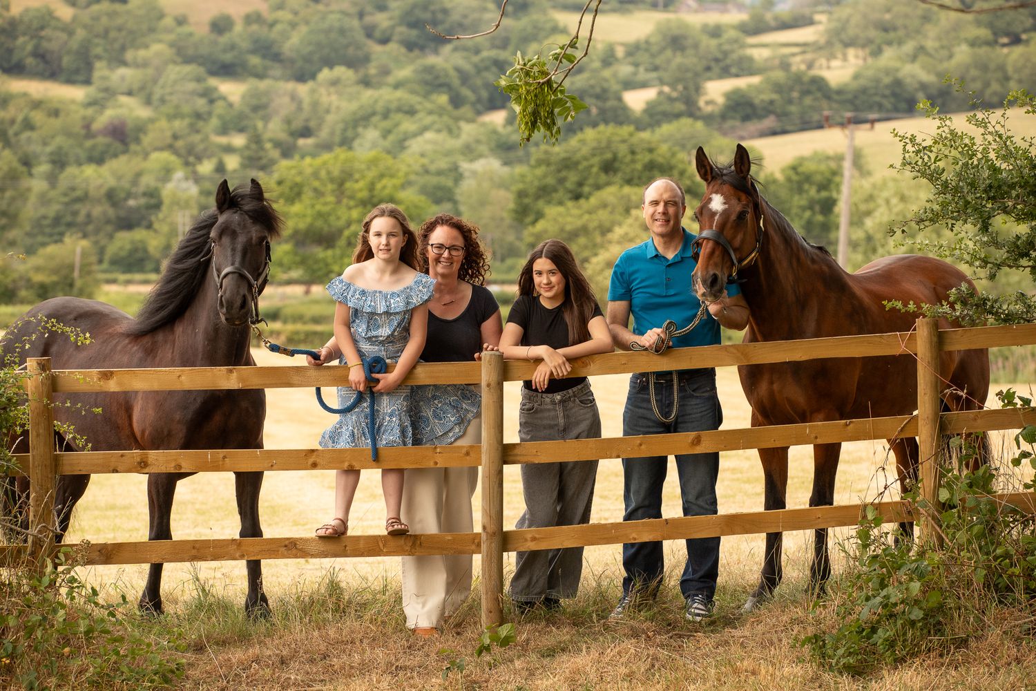 A group poses with horses along a tree-lined path during a sunny autumn day for outdoor photos.