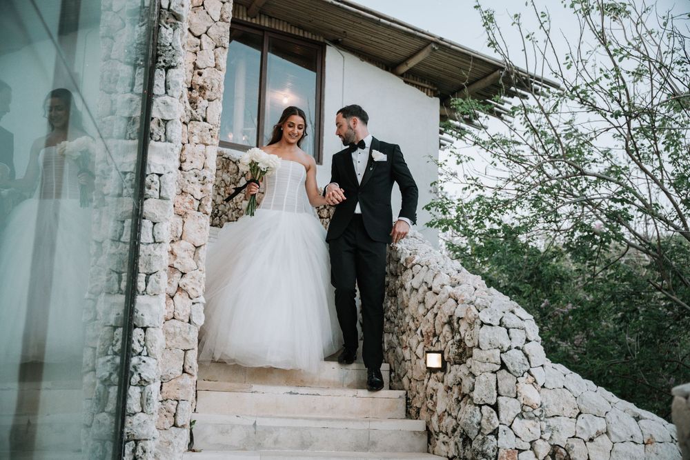 A bride and groom share an intimate moment in front of rustic stone pillars at an outdoor wedding venue.