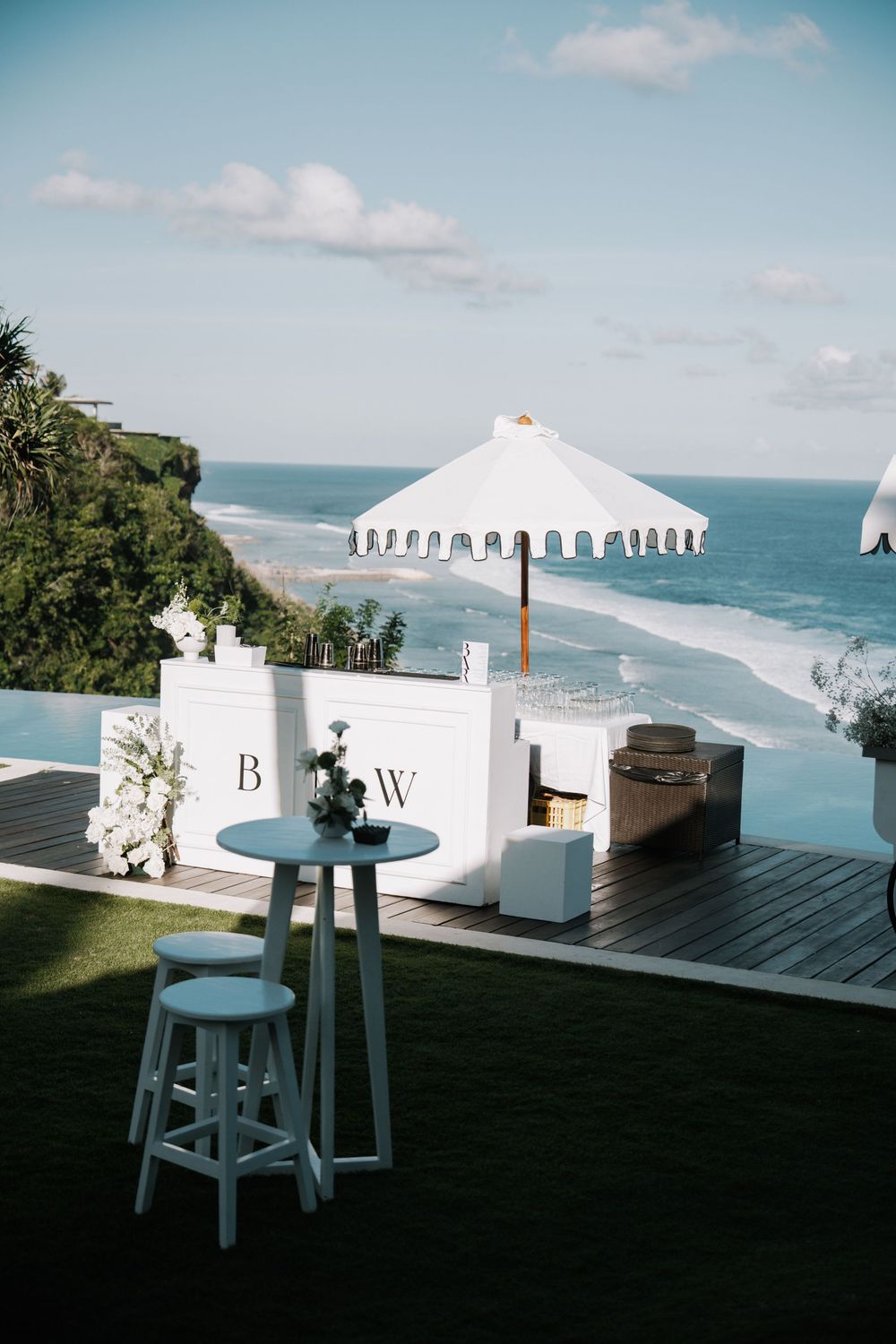 White wedding tent and furniture set up on an oceanfront lawn with stunning coastal views and turquoise waters.