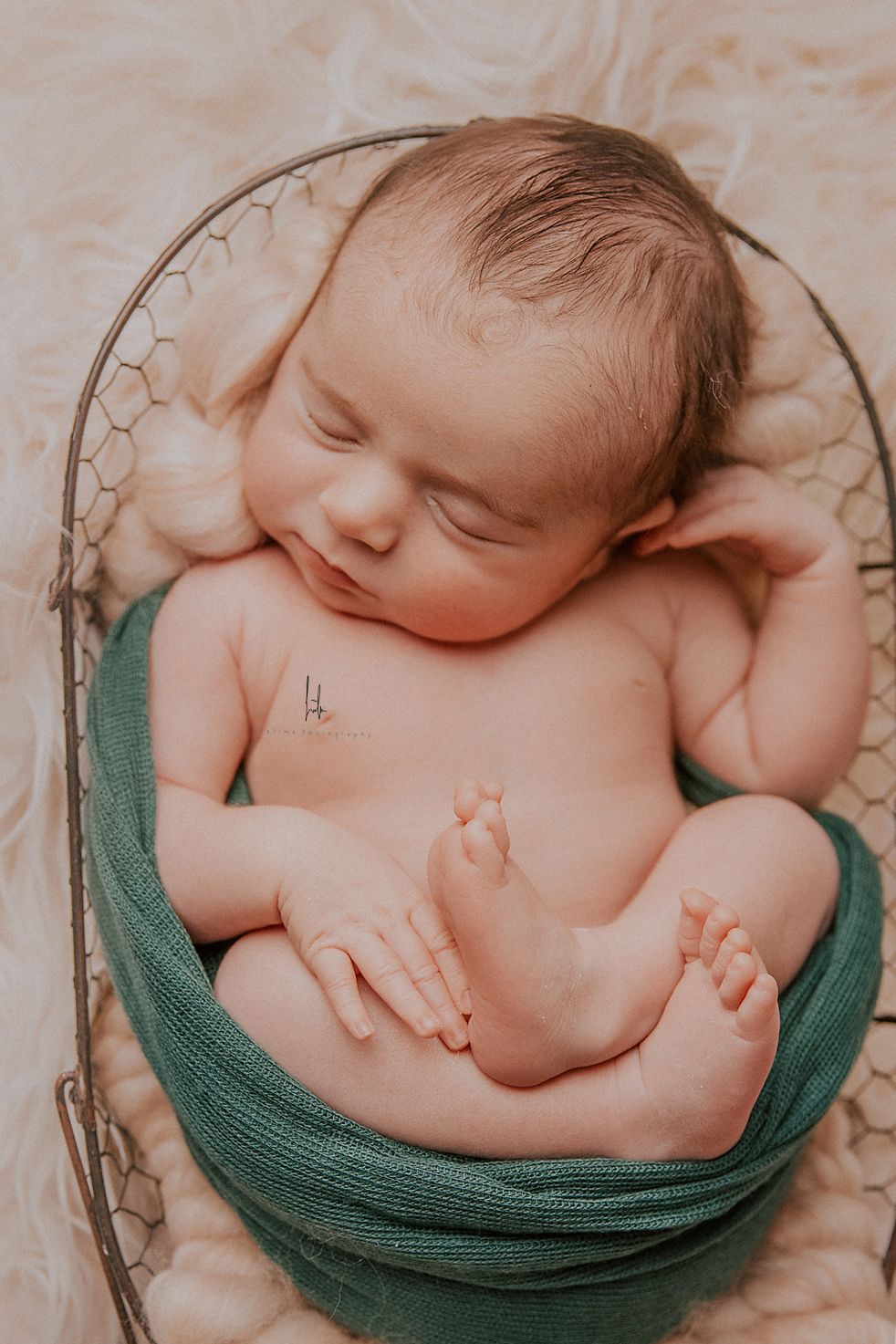 Peaceful sleeping newborn baby nestled in soft teal wrap during professional photography session.