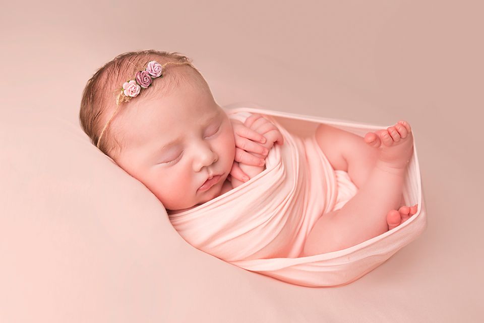 A collection of peaceful newborn portraits in soft pink tones showing a sleeping baby wrapped in delicate fabric.