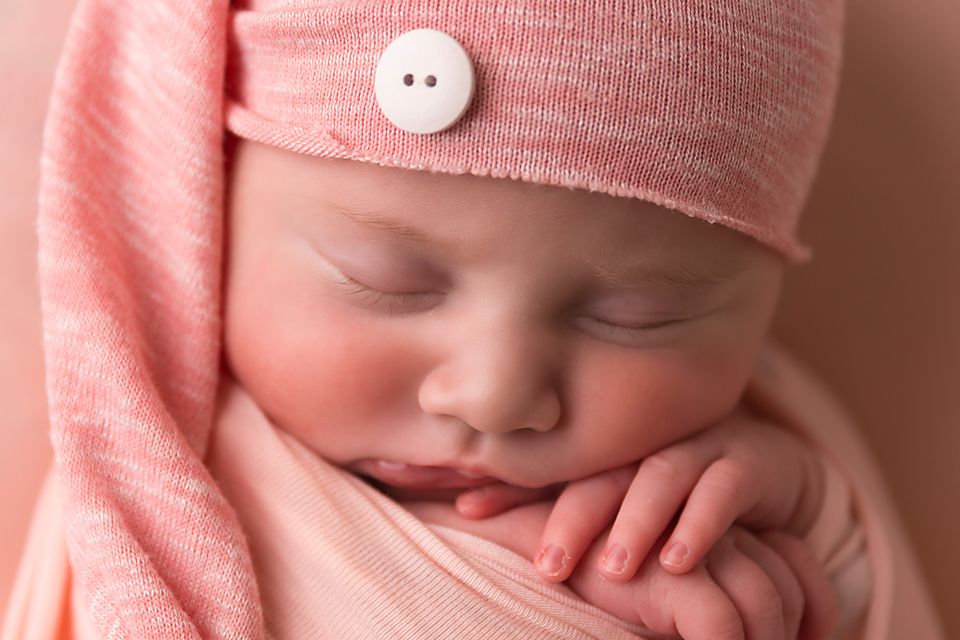 A collection of pink-tinted close-up photos showing a sleeping newborn wearing a knit cap.