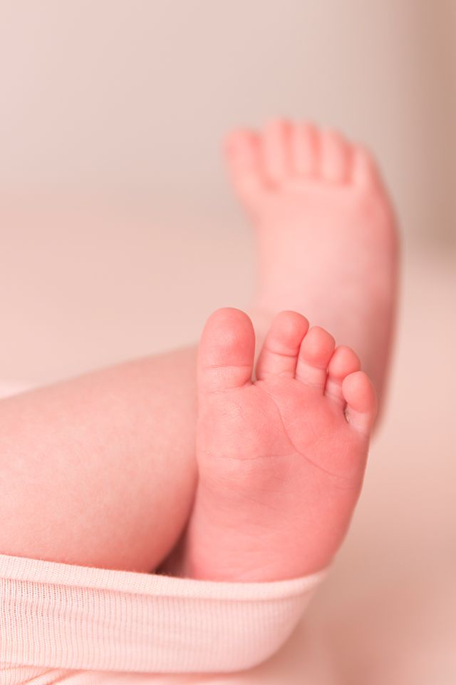 Tiny baby feet being measured with a pink measuring tape in a soft, dreamy lighting setup.