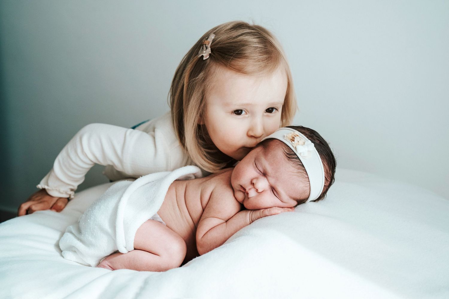 Sweet newborn baby resting on soft white bedding during professional photo session.