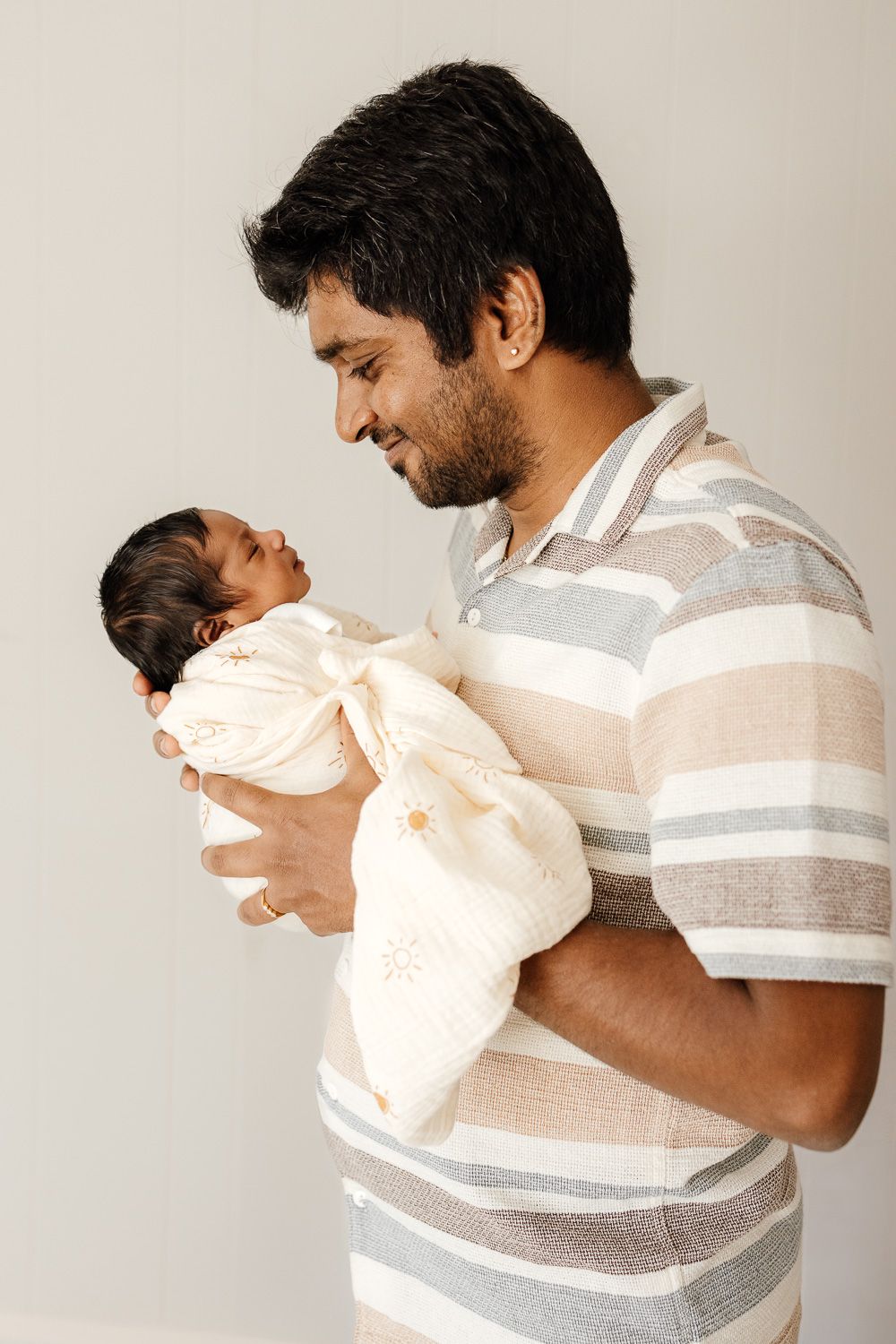 A dad smiles at his newborn baby during her in-home newborn photography session with Cindy Tucey Photography