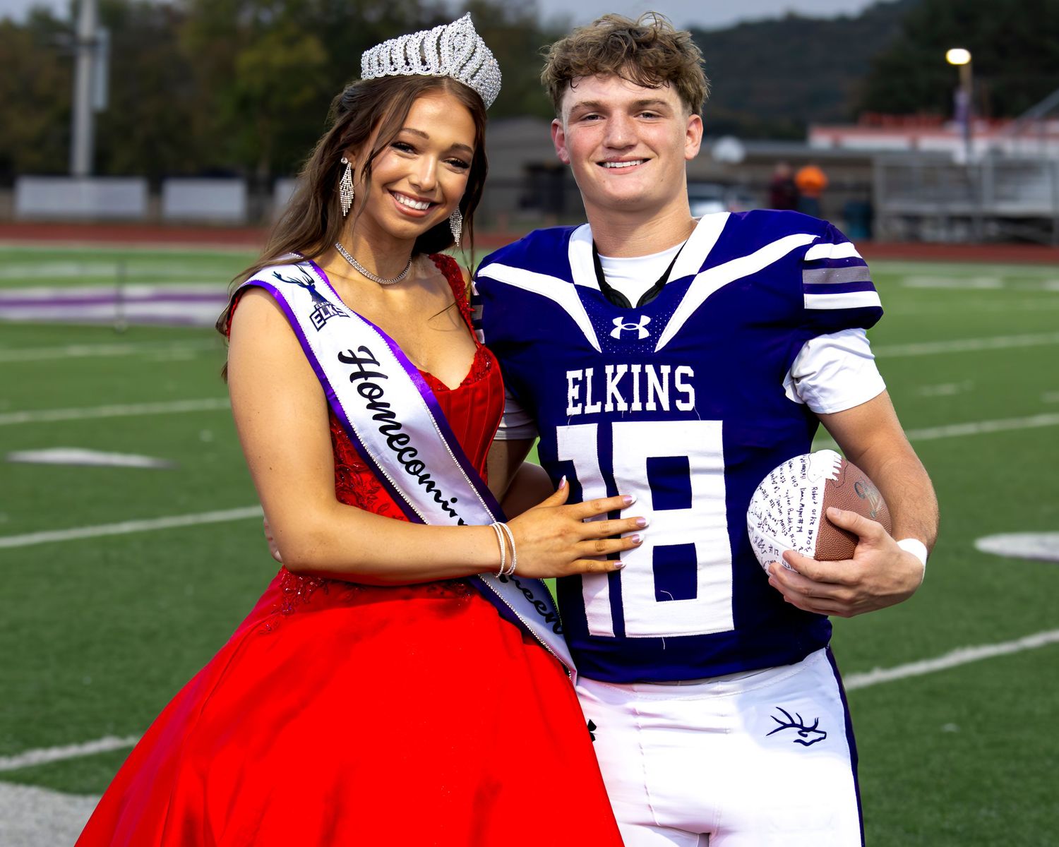 Trey Ryan and Ava Williams stand together during homecoming session wearing formal attire including red dresses and dark suits.