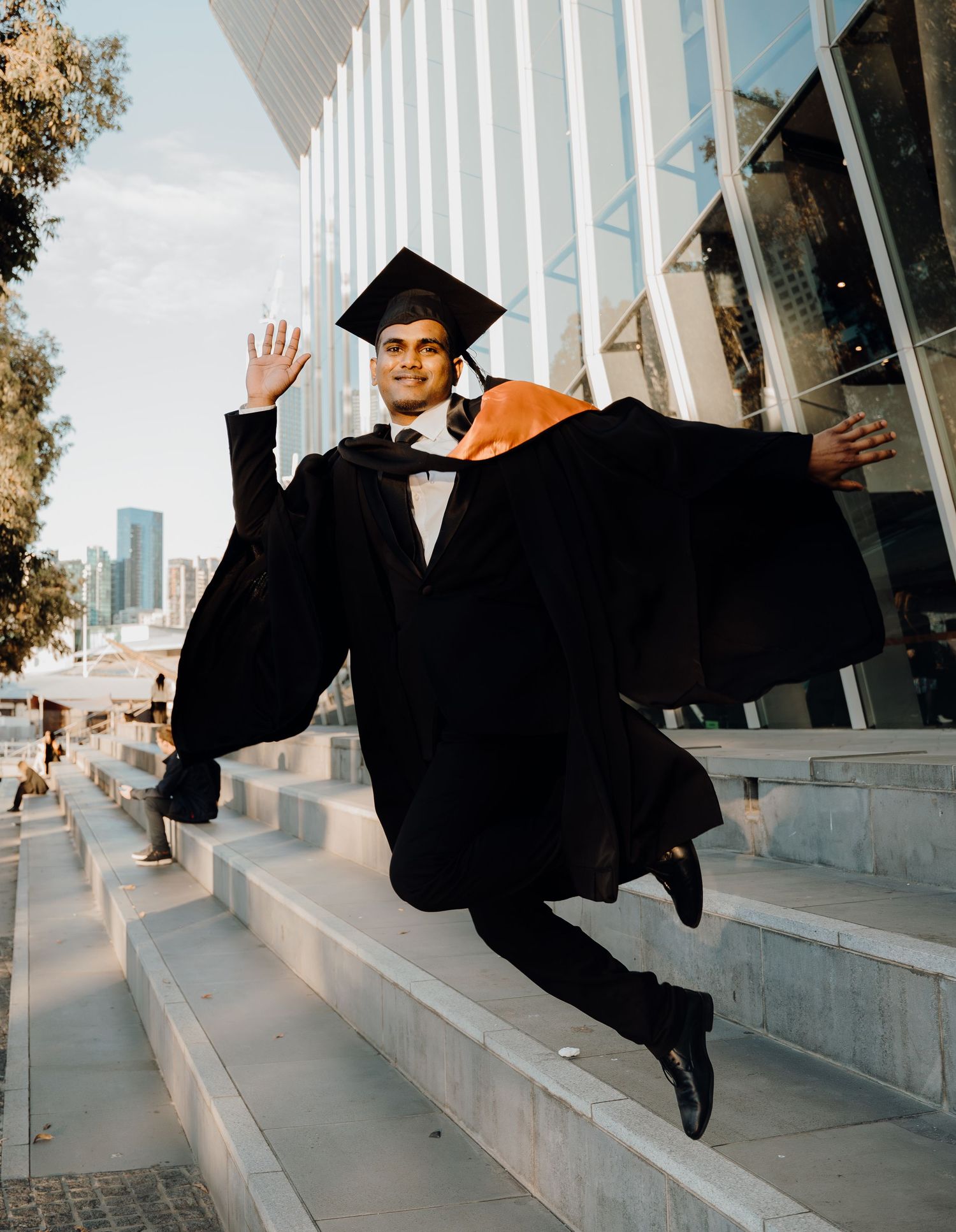 A sequence of graduation photos showing someone in black cap and gown jumping and kicking in front of a building.