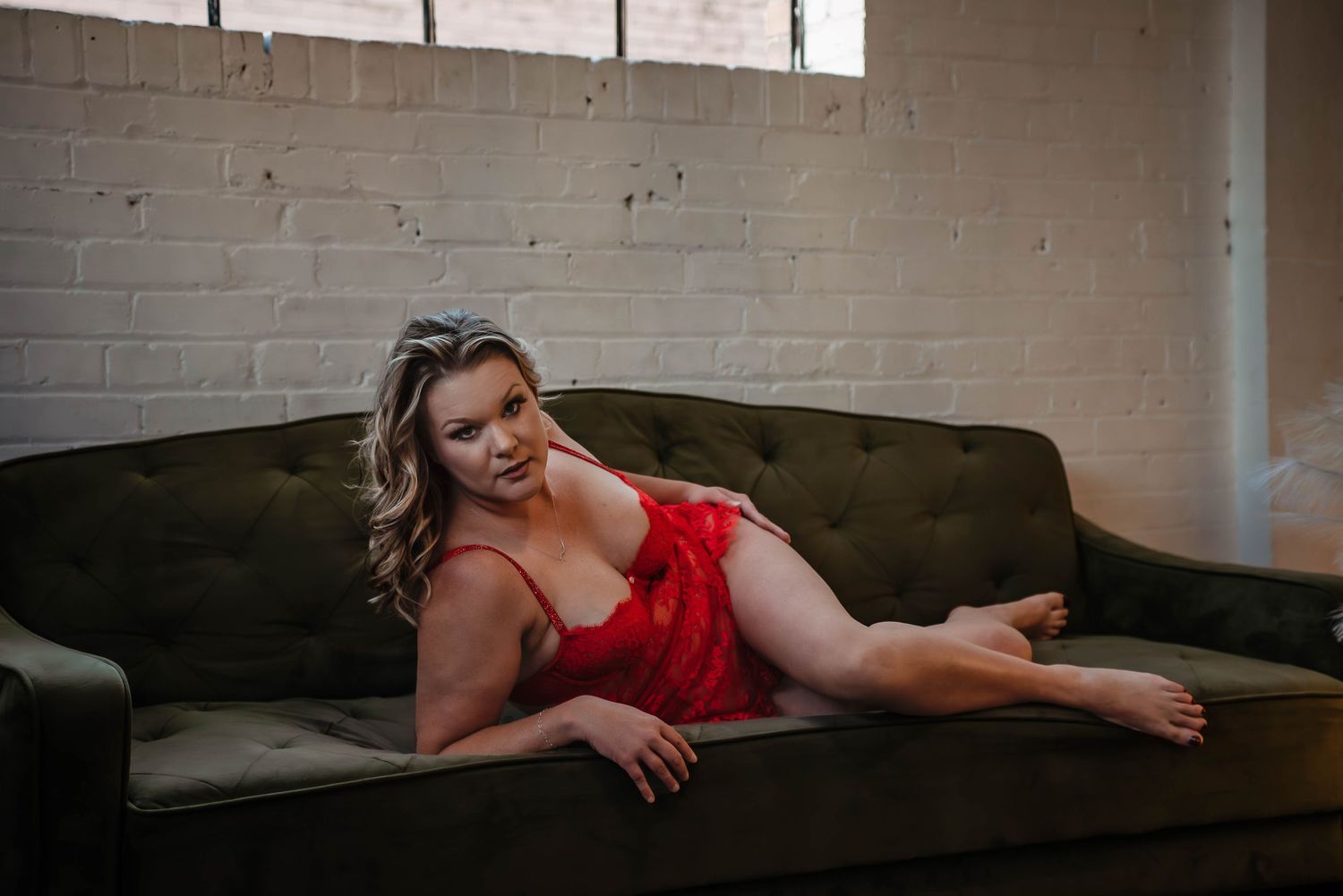 Woman being bold in red laying on a green couch staring at you in a studio at Salt Lake