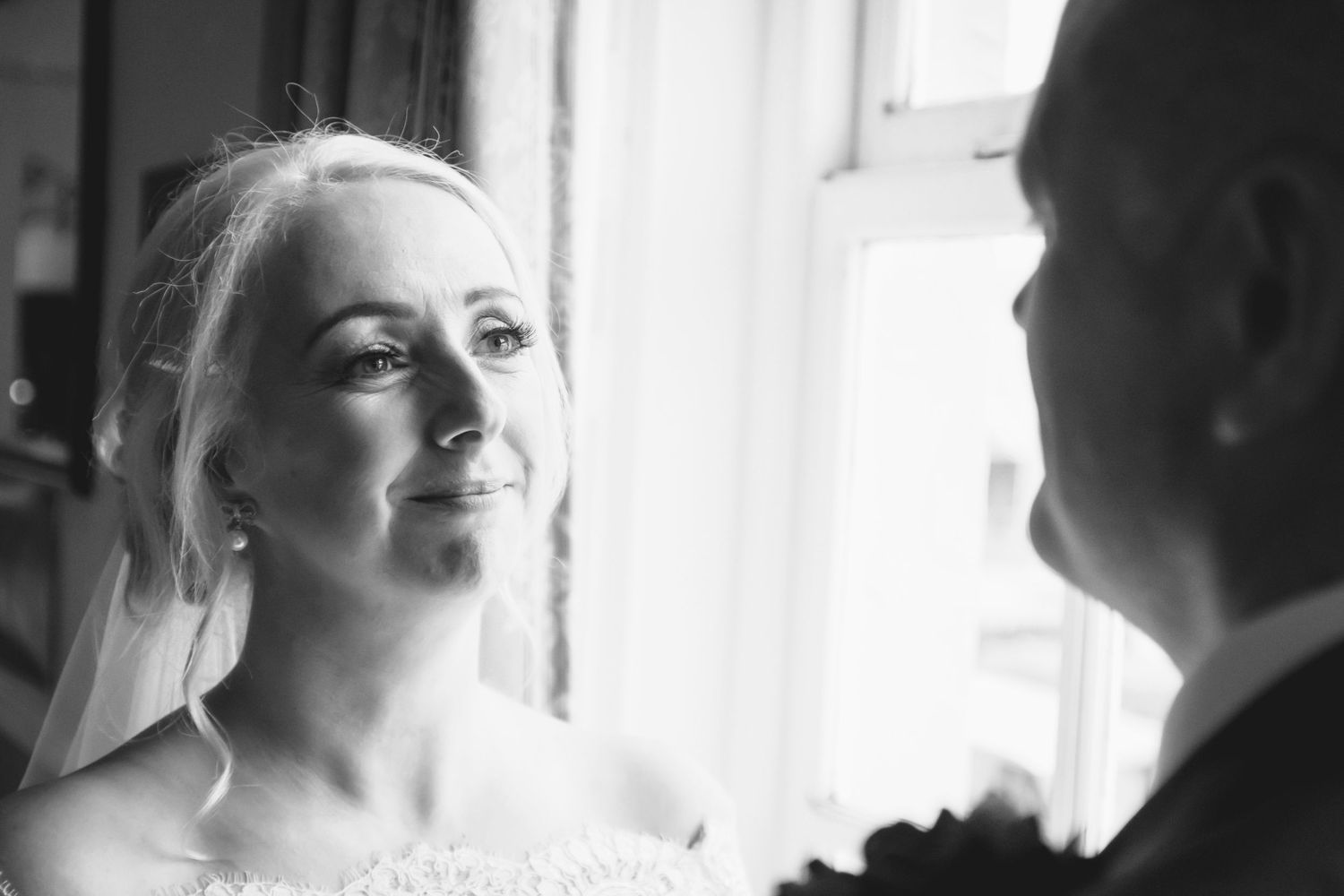 A series of black and white wedding photos showing intimate moments between a bride and groom by a window.