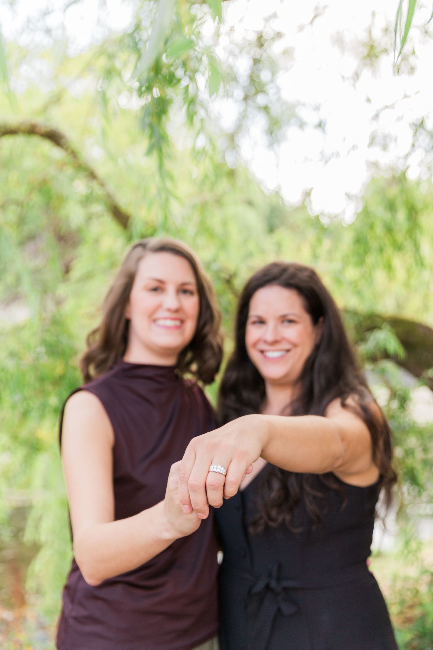 Newly engaged ladies pose holding hands, smiling with ring on show in Bibury The Cotswolds. Hayley Elizabeth photography