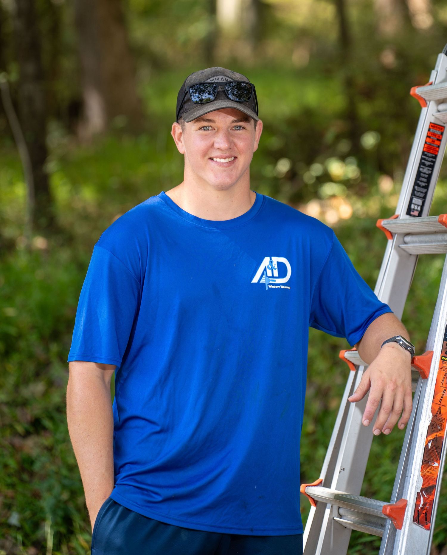 Professional service worker in blue uniform and cap standing next to a ladder outdoors.