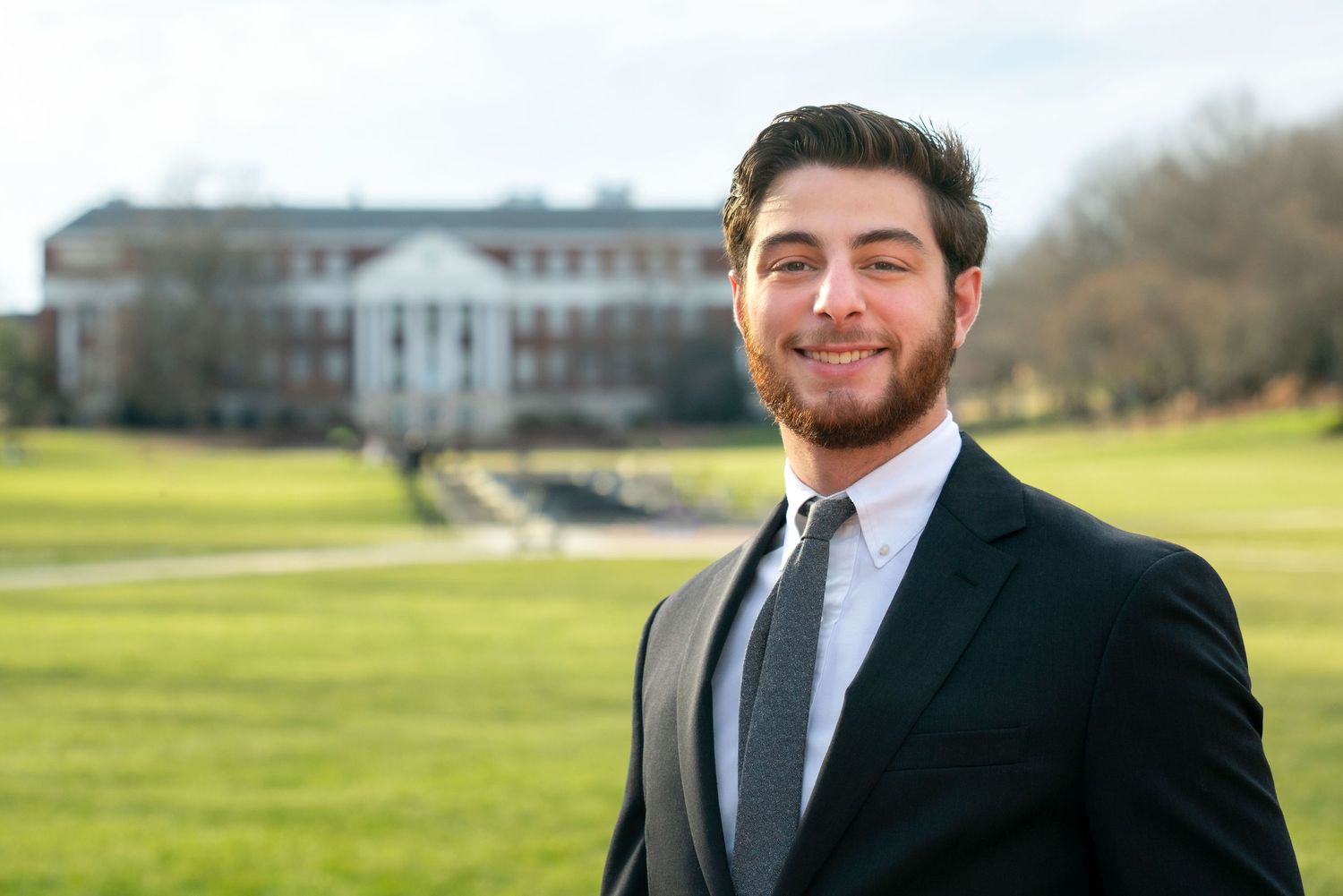 Professional outdoor portrait session in a green field with classic architecture in background.