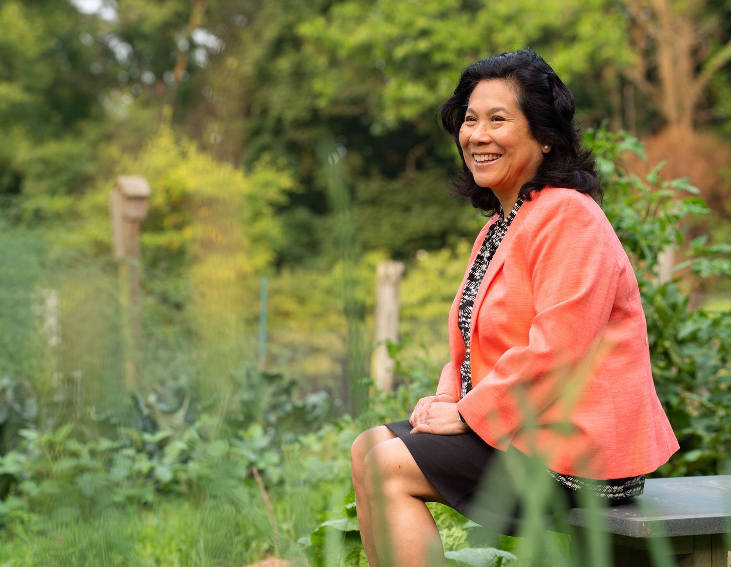 Woman in coral-colored outfit enjoying time outdoors in a natural garden setting.