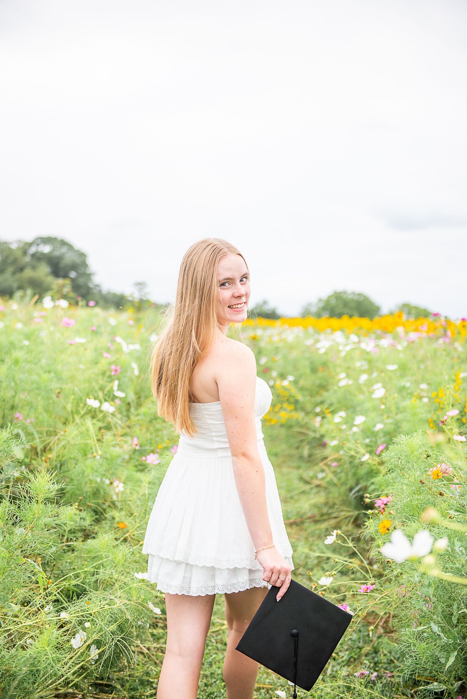 Woman in white dress poses in field of wildflowers during summer photoshoot.