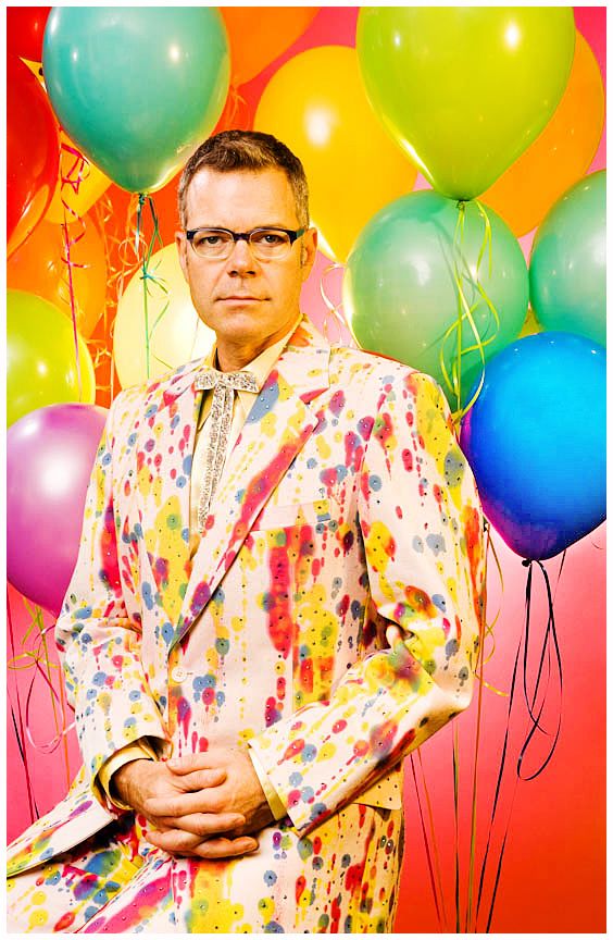 Los Angeles Brand Photographer. Colorful balloons float around a person wearing a paint-splattered jacket against a bright red background.