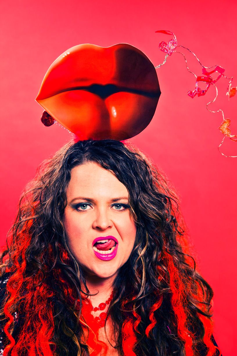 Los Angeles Brand Photographer. On a red background, woman with curly hair and lips on top of her head, has her tongue licking her top lip.
