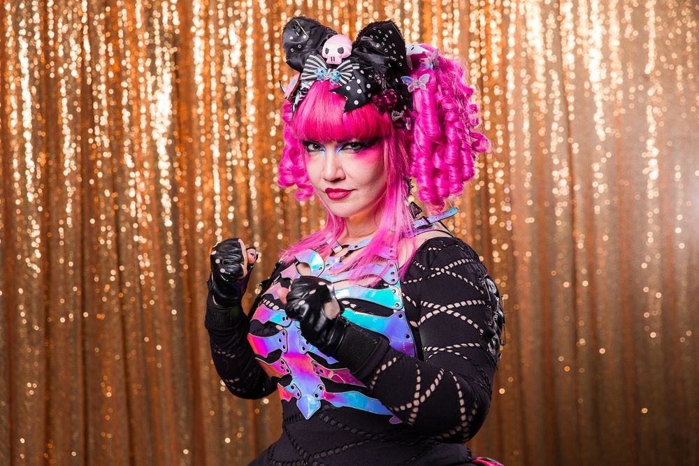 Los Angeles Brand Photographer. A performer in bright pink hair and dramatic makeup poses in front of a sparkly gold backdrop.