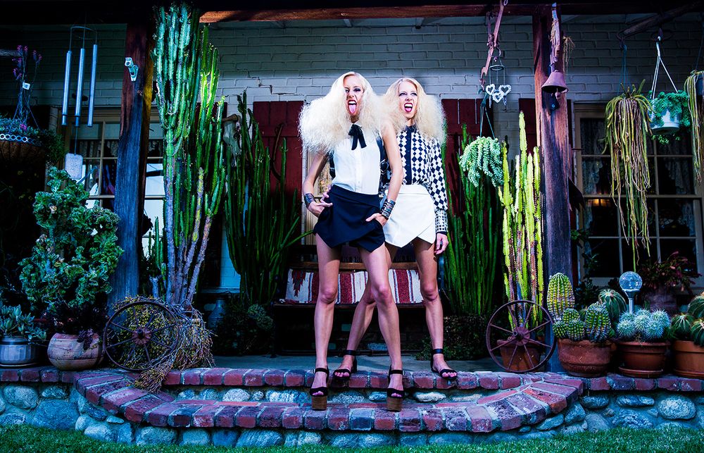 Los Angeles Brand Photographer. Two twin women pose together in front of a garden with hanging plants and cacti in an atmospheric setting.