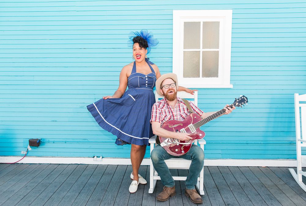 Los Angeles Brand Photographer. Against a bright blue wall one singer has a blue dress & the other singer has a guitar & western clothes.