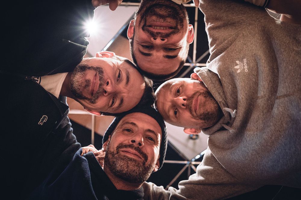 Four people huddle together in a circle looking down at the camera with smiles on their faces.