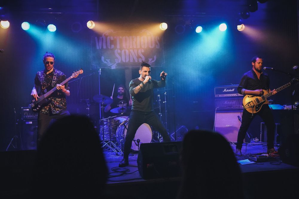 A rock band performs on stage with blue lighting, featuring musicians playing bass and guitar while a singer commands center stage.