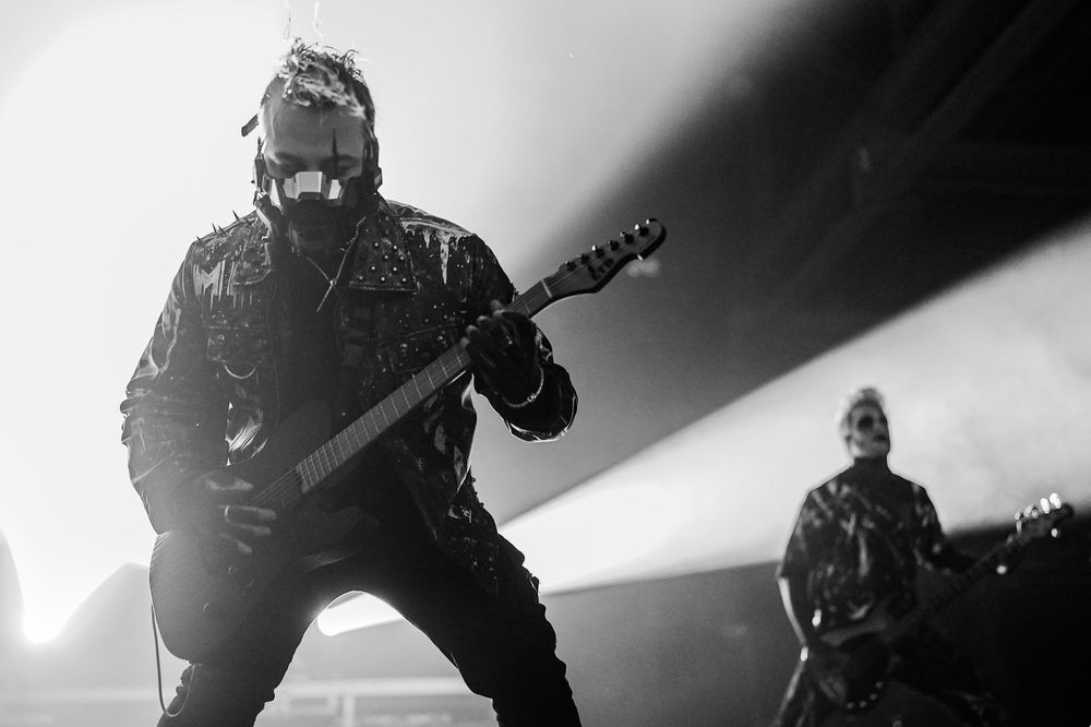 A high-contrast black and white photo of a rock band performing energetically on stage during a concert.