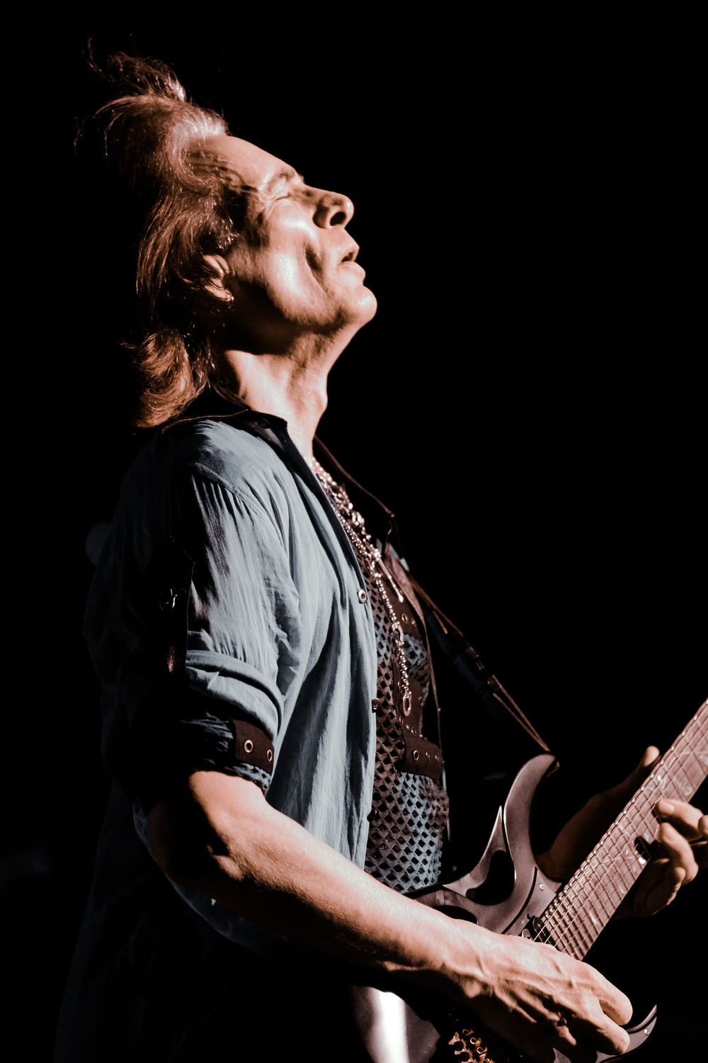 A musician performs passionately on stage with a guitar against a dark background in dramatic lighting.