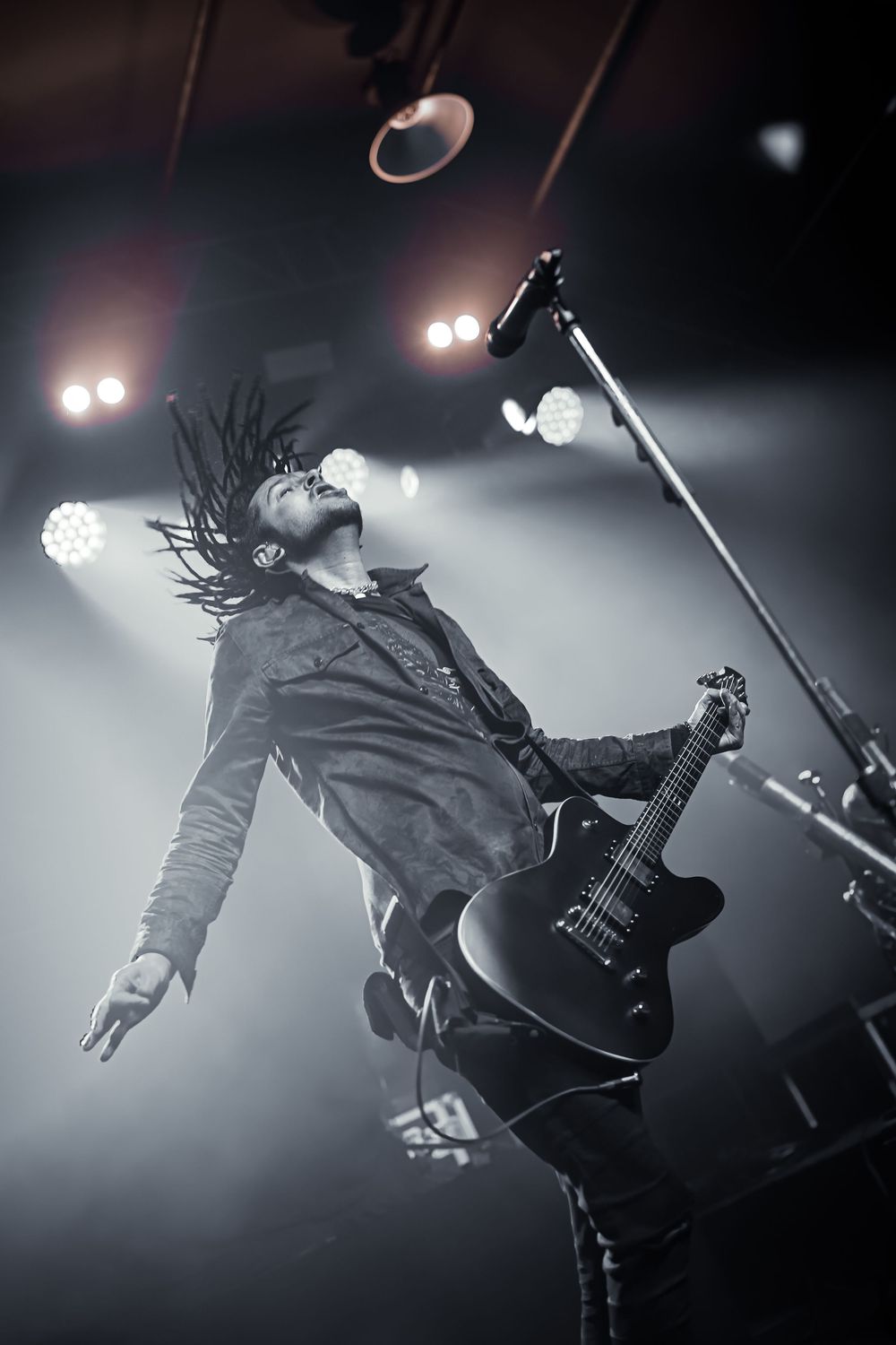 Dramatic black and white concert photo of a guitarist performing on stage with hair in motion and moody lighting.